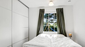 A bedroom with a bed, a window with curtains, a bedside lamp, and a view of a playground outside.