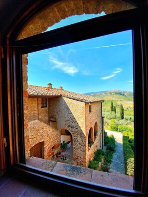 Un edificio rústico de piedra con tejado de baldosas, ventanas arqueadas y un patio con plantas en macetas.