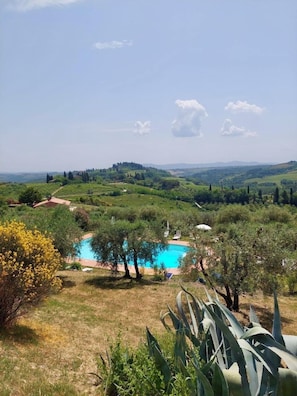 Una piscina circondata dal verde, cielo sereno e colline in lontananza.