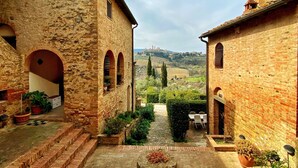 A courtyard with stone walls, a central seating area, and a view of distant hills. - Montagnana Country House - Relax and stunning view (San Gimignano)