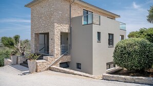 Et moderne hus i to etager med facade i sten og beton, en balkon og et lille haveområde med plantekasser.