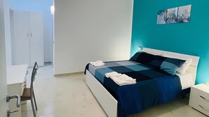 A modern bedroom with a bed, bedside tables, a desk, and a chair. - Colorado Blue, serenity inspired by the soothing tones of the sky and sea. (Zungoli)