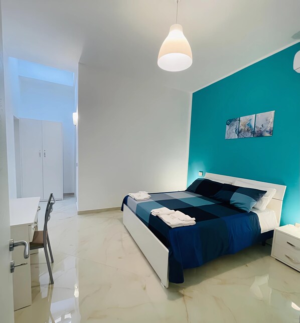 A modern bedroom with a bed, bedside tables, a desk, and a chair. - Colorado Blue, serenity inspired by the soothing tones of the sky and sea. (Zungoli)