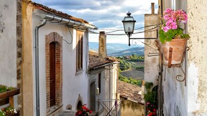 A narrow stone staircase leading to a building with a rustic facade, a metal lantern, and a flower pot on the wall. - Colorado Blue, serenity inspired by the soothing tones of the sky and sea. (Zungoli)