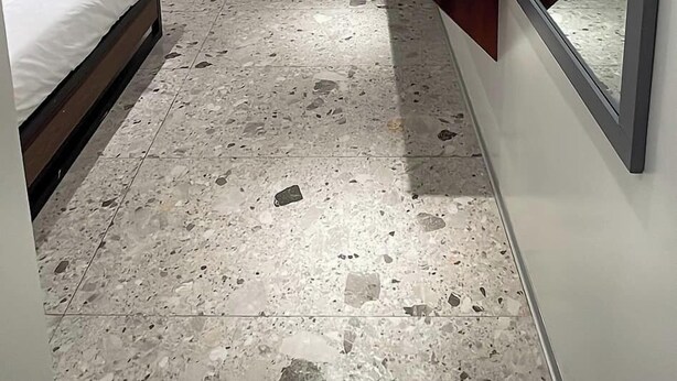 Un dormitorio pequeño y moderno con una cama, un espejo, un banco de madera y un cubo de basura.