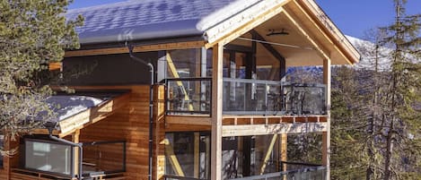 Une cabane en bois dotée d’un balcon en verre et d’un toit recouvert de neige.