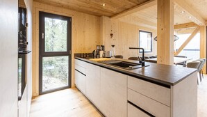 Une cuisine moderne avec des poutres en bois, une grande fenêtre et un coin repas offrant une vue sur l’extérieur.