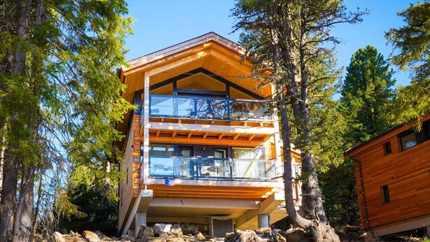 Une cabane moderne en bois, à plusieurs étages, entourée d’arbres.
