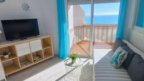 A balcony with a view of the sea, a TV on a wooden stand, a sofa with cushions, and a small table with a plant. - Apartment with terrace and sea views (Benalmádena)