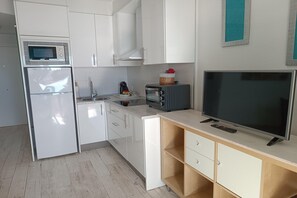 A compact kitchen with a microwave, refrigerator, toaster, and a flat-screen TV on a wooden counter.