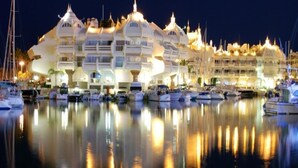 A marina with yachts and a large, uniquely designed hotel with multiple balconies and a reflective water surface.