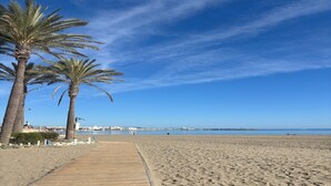 A wooden boardwalk leading to a sandy beach with palm trees and a clear blue sky.