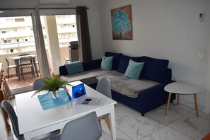 Uma sala de estar com sofá, mesinha, planta em vaso e um quadro na parede.