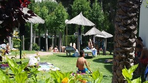 An outdoor area with thatched umbrellas, palm trees, and people relaxing on the grass. - Apartment with beach and garden views (Benalmádena)