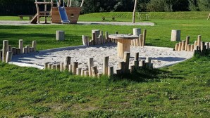 A playground with a wooden ship-shaped play structure and a sandpit surrounded by wooden posts.
