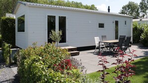A small, white mobile home with a patio area featuring a table and chairs.