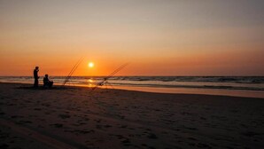 A beach at sunset with two people fishing.