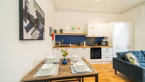Una cocina moderna con armarios blancos, una mesa de comedor para cuatro personas y un sofá azul en la sala.