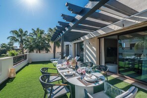 Eine Dachterrasse mit Essbereich, Palmen und einer Pergola.