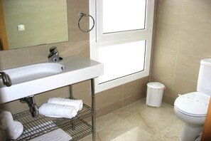 A bathroom with a white sink, a toilet, and a trash bin.