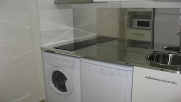 Cocina compacta con lavadora y secadora integradas, microondas y pileta de acero inoxidable.