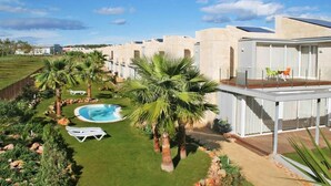 Un hotel moderno con piscina, palmeras y una zona exterior cubierta con sillones de descanso.