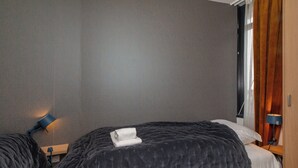 Habitación de hotel con cama, mesita de noche, lámpara y ventana con cortinas.