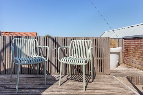 Two outdoor chairs on a wooden deck with a wooden fence and a brick wall in the background.