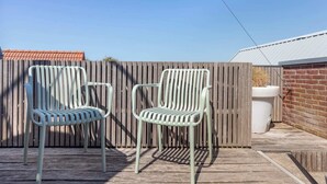 Dos sillas metálicas al aire libre sobre una terraza de madera, con una valla de madera y un muro de ladrillo al fondo.