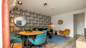 Una sala moderna con papel tapiz floral, una mesa redonda, sillas color turquesa, un sillón amarillo y una alfombra circular.