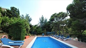 Ein rechteckiger Swimmingpool mit einer gefliesten Kante, umgeben von blauen Liegestühlen und einer Steindeck.