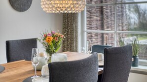 A dining area with a wooden table, grey upholstered chairs, a vase with flowers, and a hanging light fixture.