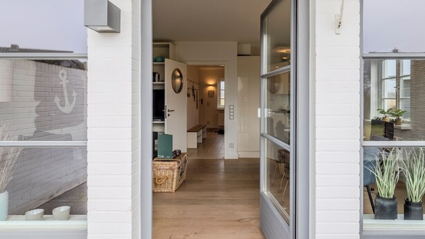 A modern interior with a wooden floor, a glass door leading to a hallway, and a white brick wall.