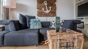 A modern living room with a grey sofa, a wicker coffee table, and a mounted wooden anchor decoration.