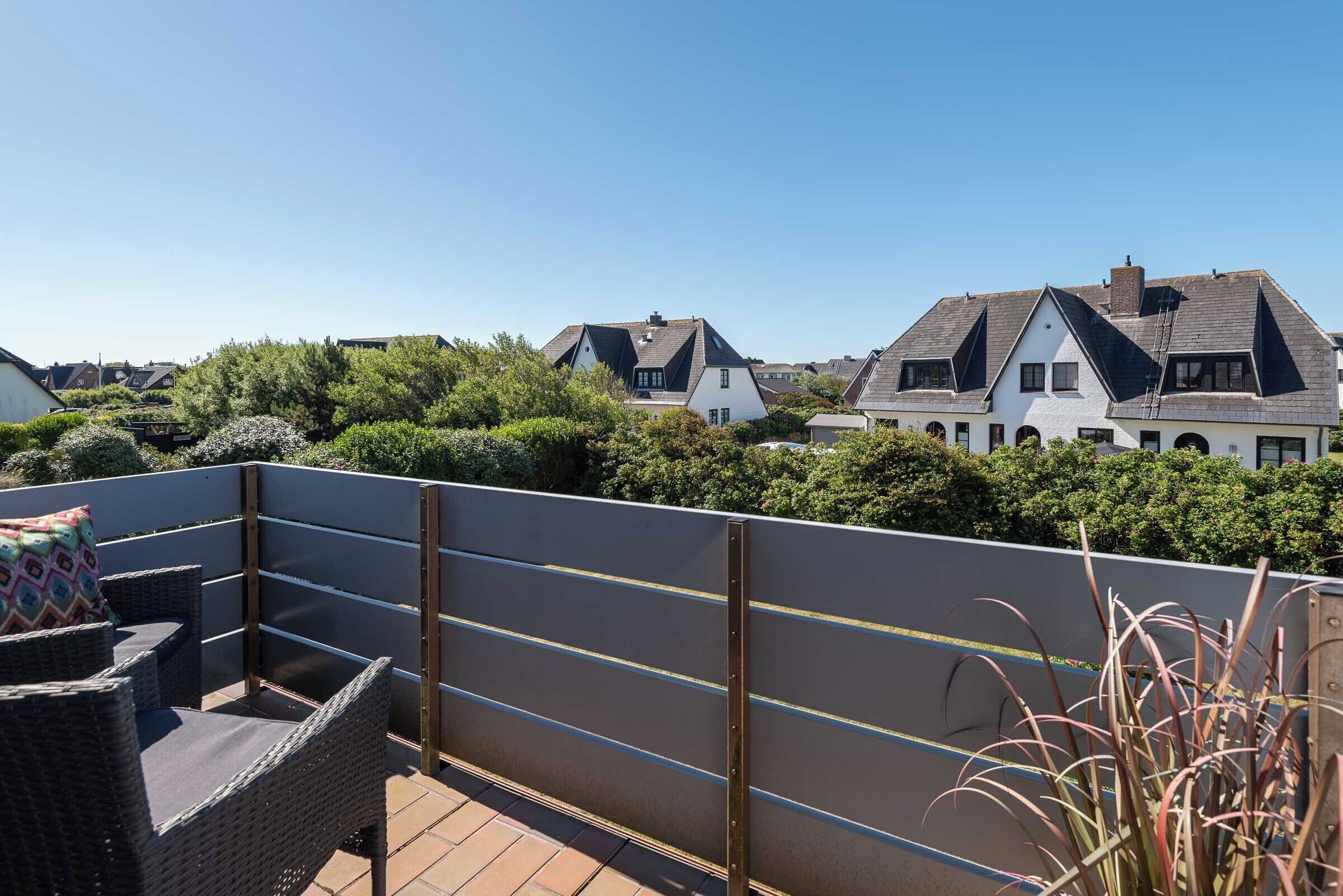 A rooftop terrace with wicker furniture and a view of neighboring houses.