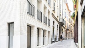 A narrow cobblestone street lined with multi-story buildings, featuring balconies and a mix of architectural styles.
