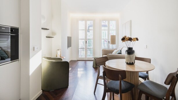 A modern kitchen with a dining area, a sofa, and a vase with flowers.