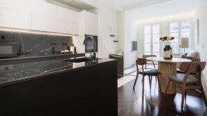 A modern kitchen with a marble countertop, stainless steel appliances, and a dining area with a round wooden table and chairs.