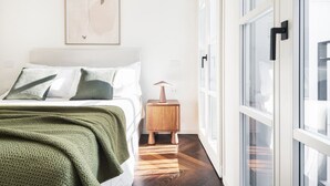 A bedroom with a bed, a bedside table, a lamp, and a window.