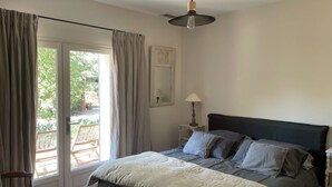 Ein Schlafzimmer mit Bett, Nachttisch, Lampe, Sessel und einer Schiebetür zu einem Außenbereich.