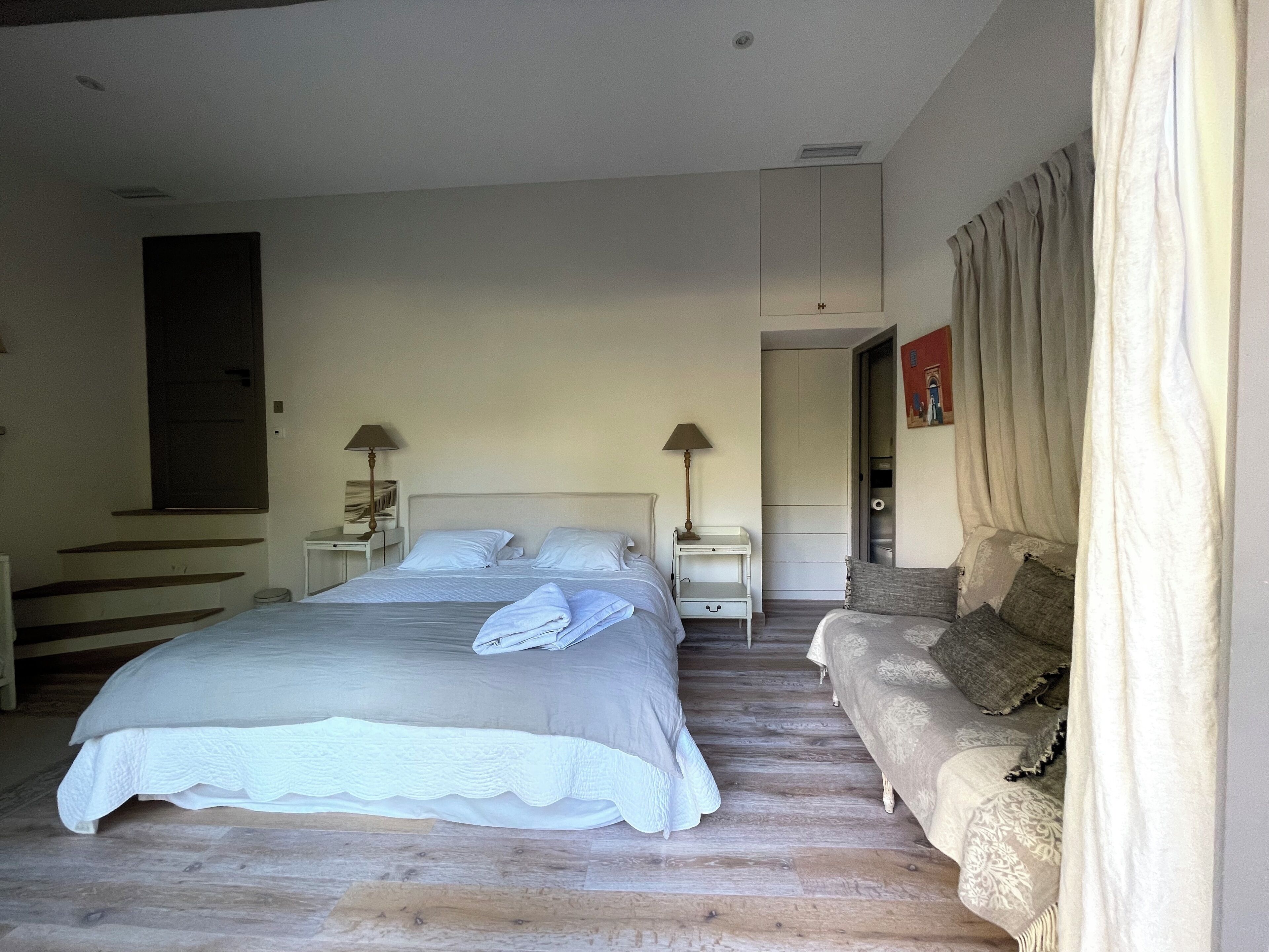 Ein Schlafzimmer mit einem großen Bett, zwei Nachttischen, einem Beistelltisch, einer Couch und einer Tür zu einem anderen Raum.