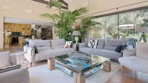 Ein geräumiges Wohnzimmer mit einem Glastisch, grauen Sofas und großen Fenstern mit Blick ins Freie.