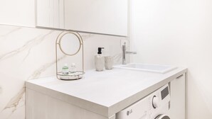 Ein modernes Badezimmer mit Marmorplatte, Waschbecken, Spiegel und integrierter Waschmaschine.