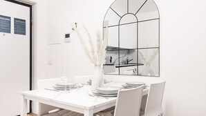 Ein weißer Esstisch mit Stühlen, eine Vase mit Pampasgras und ein Spiegel mit geometrischem Muster an der Wand.