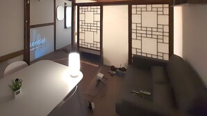 A room with a white table, a grey sofa, a small plant on the table, and a decorative screen with a geometric pattern. - Hyehwa 1937 (Hanok), a traditional Korean house built in 1937 (Seongbuk District)
