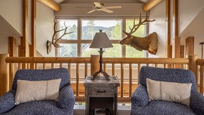 Een gezellig interieur van een chalet met twee blauwe fauteuils, een houten tafel, een lamp en gewei aan de muur.