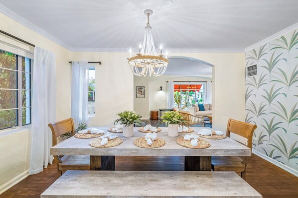 A dining room with a large table set for six, surrounded by chairs, a chandelier, and potted plants. - Timeless Elegance: Historic Estate w/ Pool, Hot Tub + Putting Green (Phoenix)