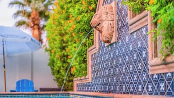 Una piscina con una pared decorativa que muestra una cabeza de león y azulejos con diseño azulado.