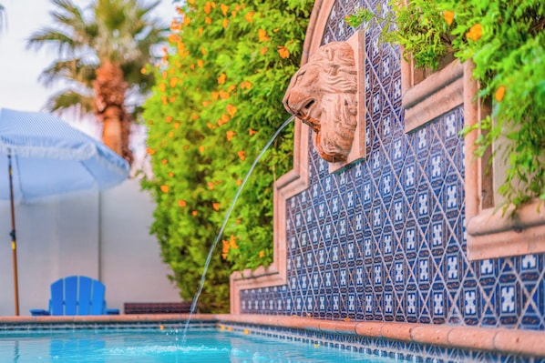 Ein Pool mit einer Zierwand, die einen Löwenkopf und blau gemusterte Fliesen zeigt.