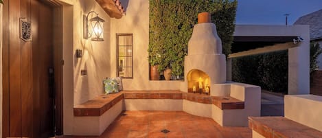 Un patio con piso de piedra, una puerta de madera, un farol en la pared y un horno de ladrillo.